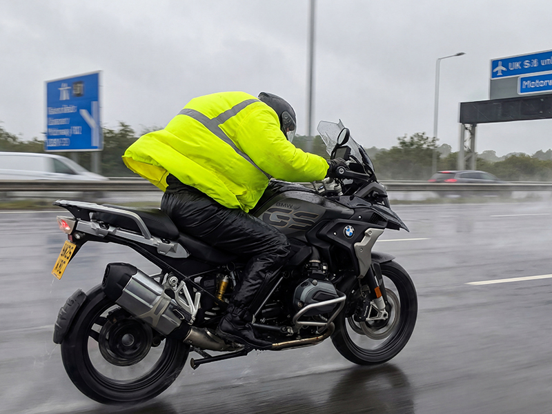 Guy riding motorcycle on motorway with flapping waterproofs